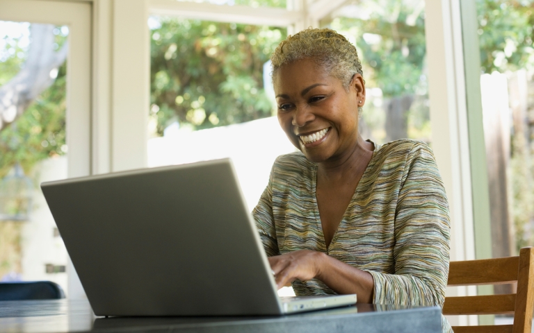 Eine schwarze Frau lächelt, während sie auf einem Laptop tippt