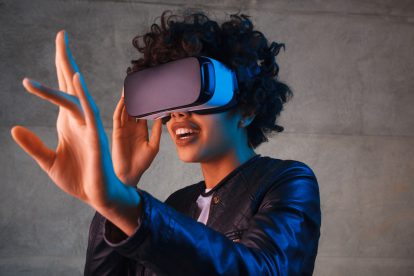 Junge Frau trägt eine Virtual-Reality-Brille und streckt ihre linke Hand aus, um zu staunen