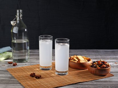 Zwei Gläser mit türkischem Raki auf einem Tisch mit Schalen mit Snacks und einer offenen Flasche Wasser im Hintergrund