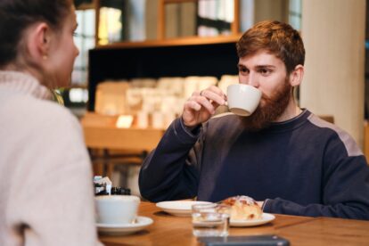 Junger bärtiger männlicher Freiberufler trinkt Kaffee in einem Berliner Café und unterhält sich mit einem Kollegen